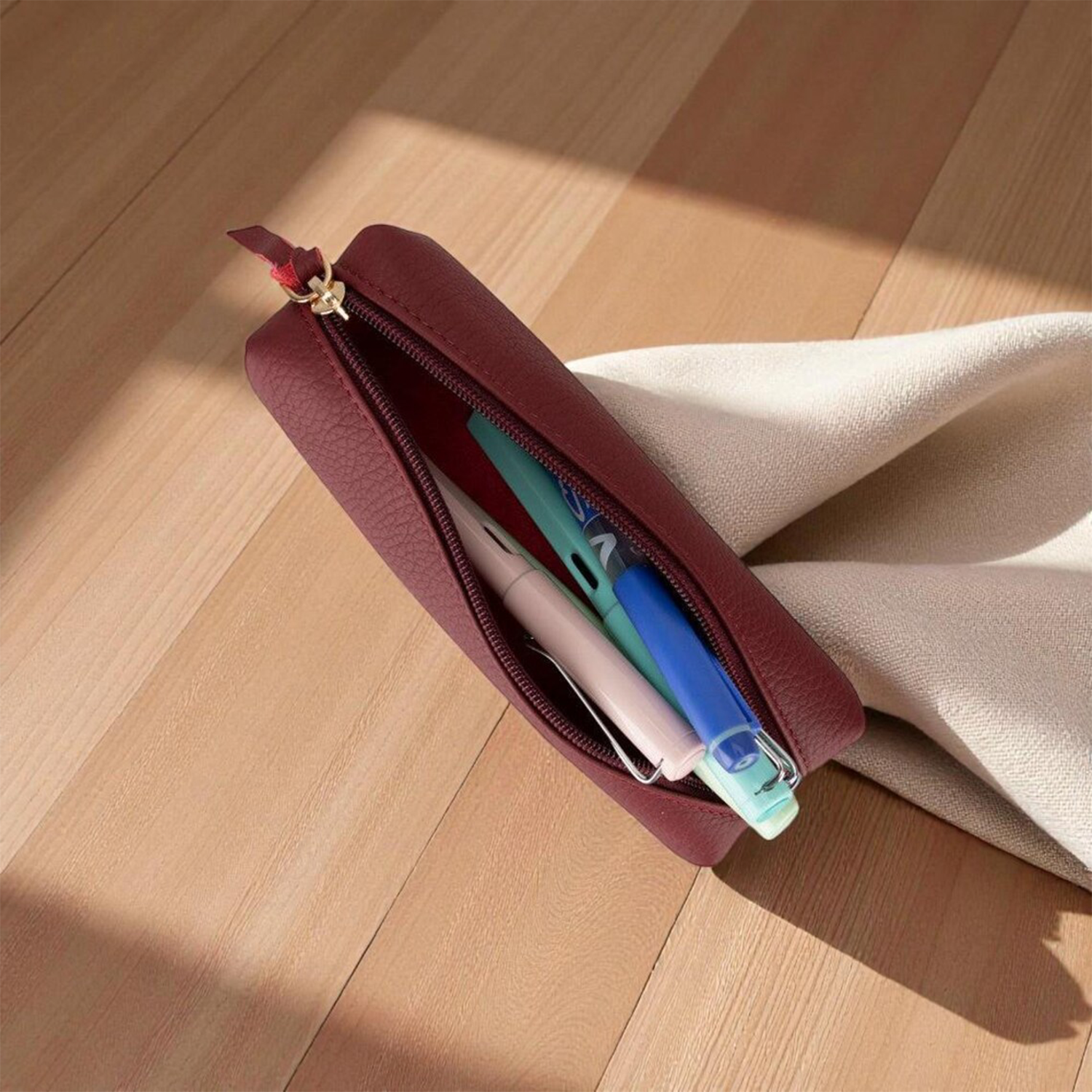 Burgundy Pebbled Textured Elongated Stationery Pouch With Full-Length Gold-Tone Zip Closure, Fabric Pull Tab And Folded Rounded End Cap Silhouette